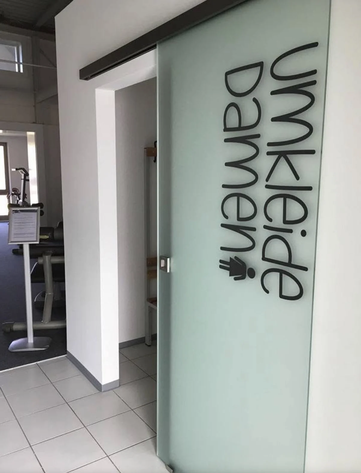 Gläserne Schiebetür zur Damenumkleide in der Praxis neben dem Trainingsbereich